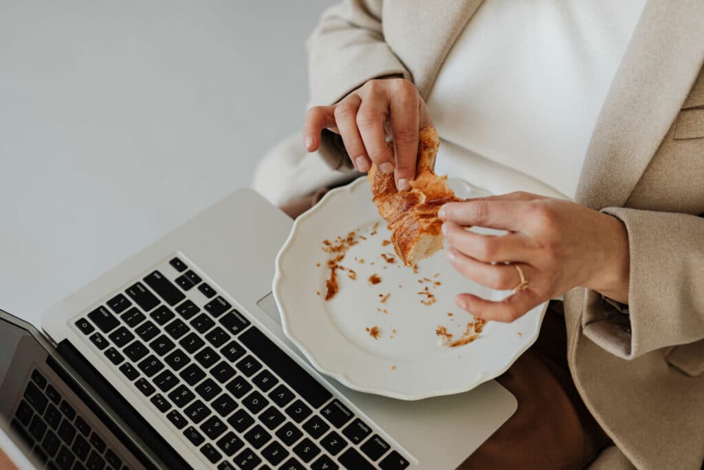 Frau vor dem Laptop, mit croissants in der Hand